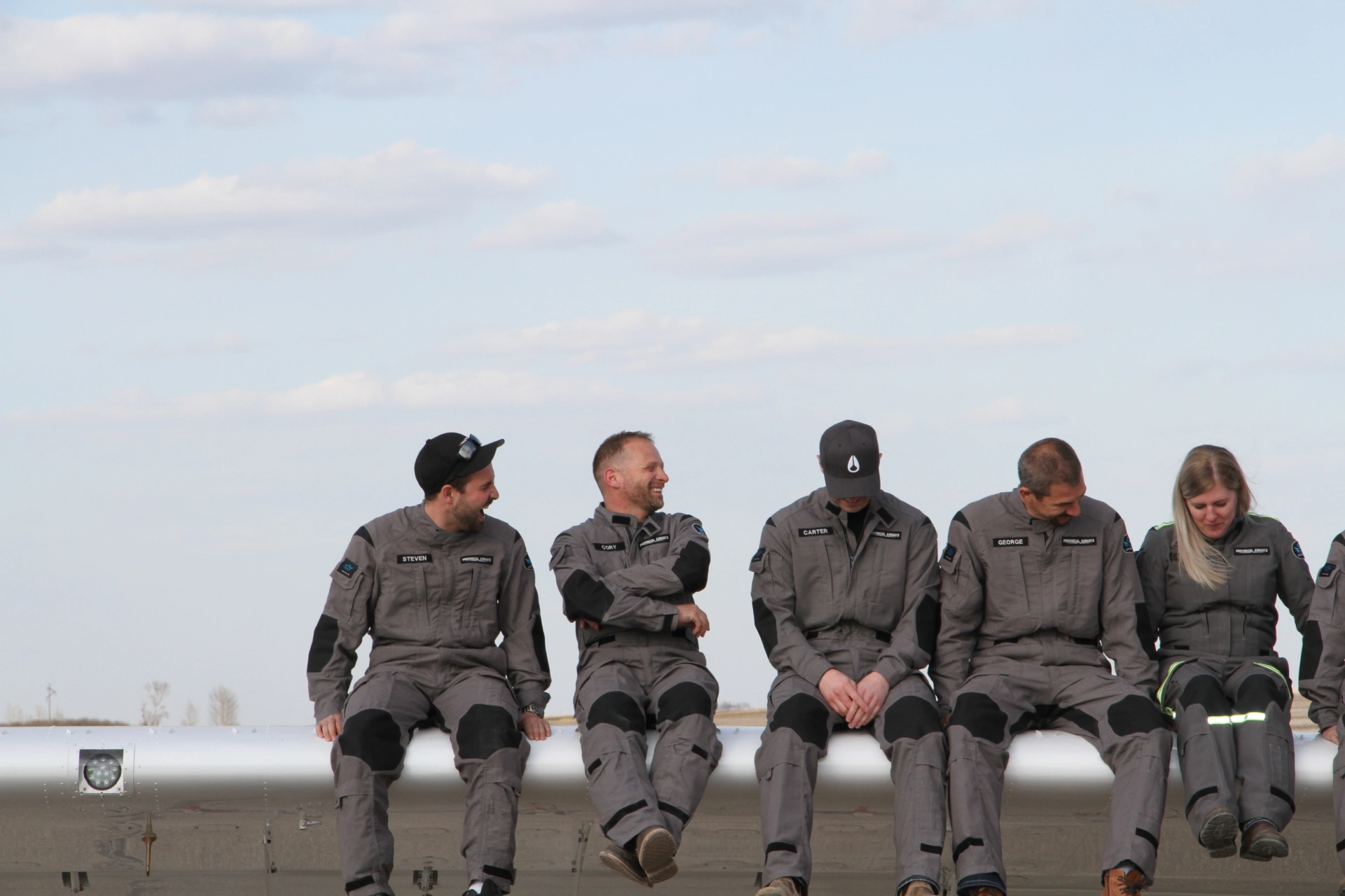 Several small private airplanes are parked in a row on an airport tarmac under a clear blue sky